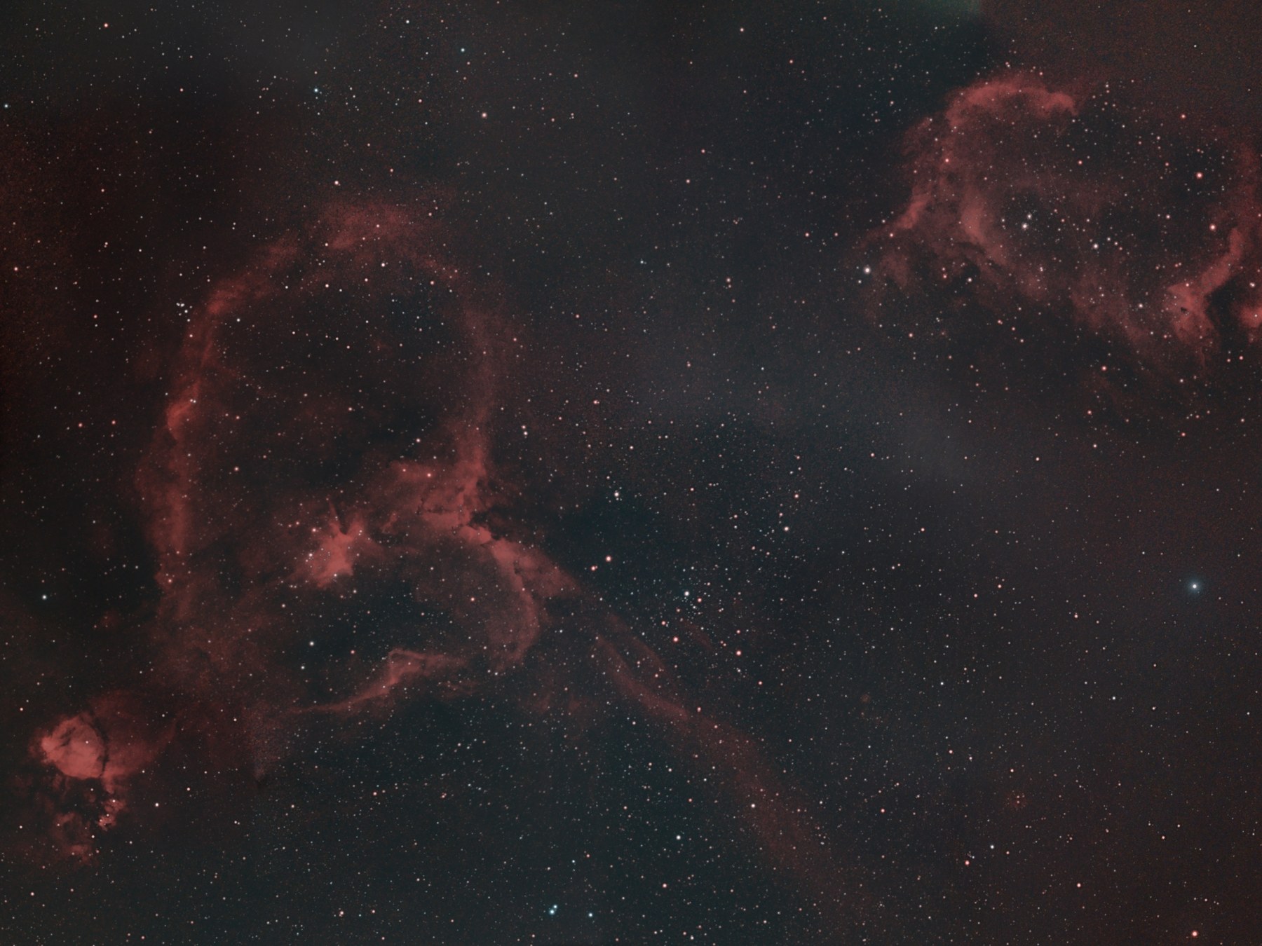 An eighteen-panel mosaic of the Heart and Soul nebulae photographed from Lakeway, Texas with two Seestar telescopes, turned so south is up: the Heart Nebula standing large at left with a long red filament trailing down and to the right, the bright Fishhead Nebula at its lower left, the Soul Nebula at upper right, and a star field between them.