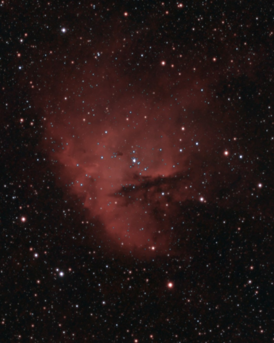 The Pacman Nebula (NGC 281) photographed from Lakeway, Texas with a ZWO Seestar S50 Pro — a round red emission nebula with a dark dust lane cutting in like an open mouth, around a cluster of blue-white young stars.